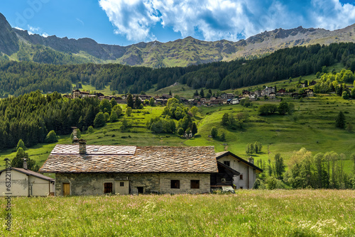 Rural house on the meadow and small village on the mountain slope in Aosta Valley, Italy.
