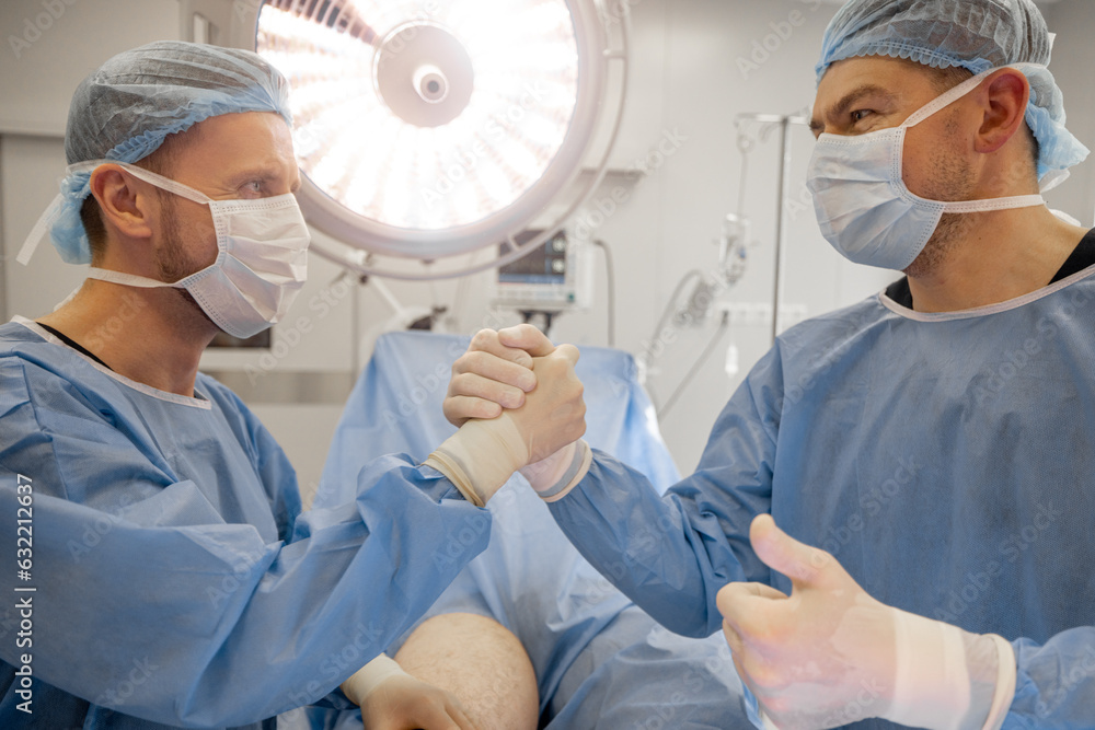 Surgeons shaking hands after successful operation in operating room. Concept of teamwork and success in surgery Surgeons shaking hands after successful operation in operating room. Concept of teamwork and success in surgery