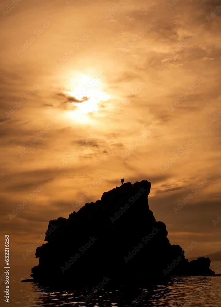 silhouette of a man climbing a mountain rising out of the sea against the backlight of the sunset with the sky overcast