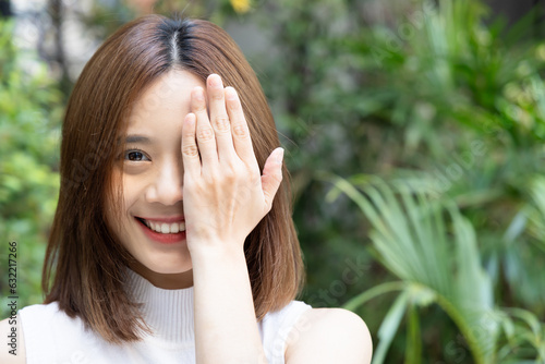 Happy smiling young woman looking with one eye, covering another eye