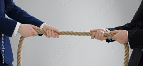 Dispute concept. Men pulling rope on light grey background, closeup