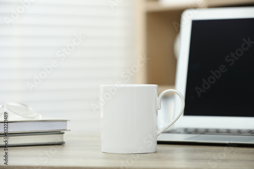White ceramic mug, notebooks and laptop on wooden table indoors