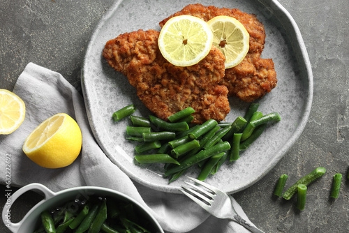 Tasty schnitzels served with lemon and green beans on grey table, flat lay