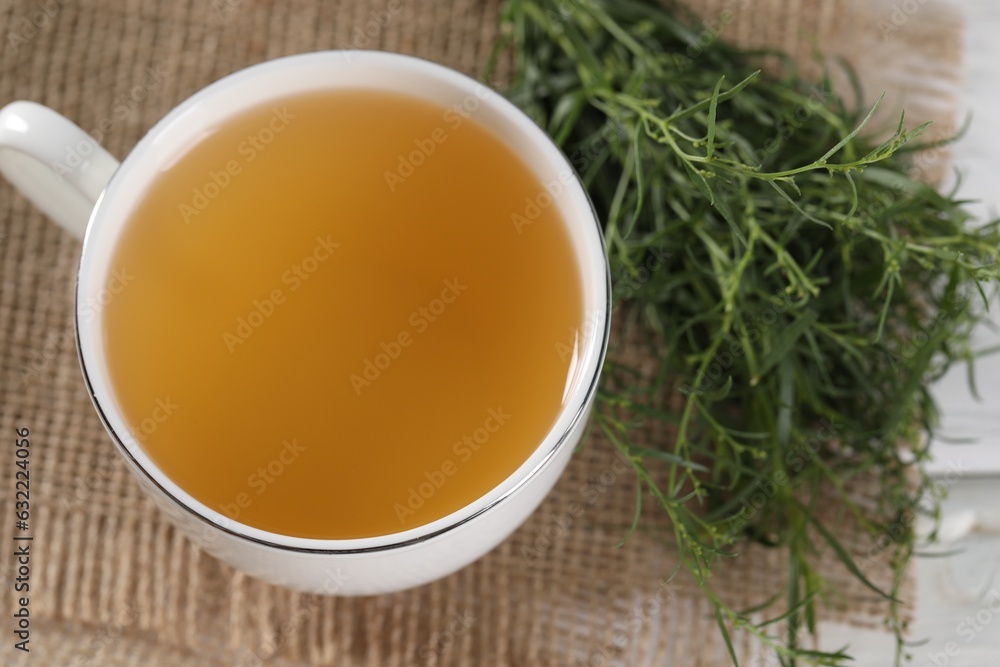 Aromatic herbal tea and fresh tarragon sprigs on table, above view Aromatic herbal tea and fresh tarragon sprigs on table, above view
