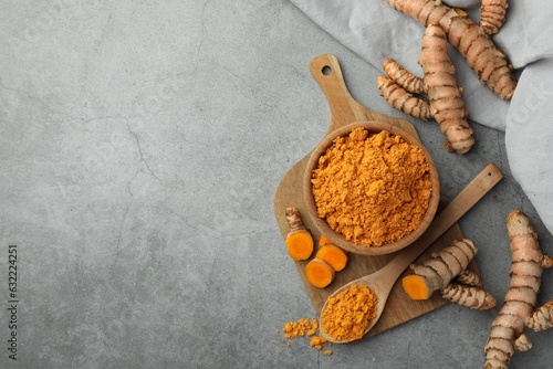 Aromatic turmeric powder and raw roots on grey table  flat lay. Space for text