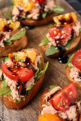 Delicious bruschettas with balsamic vinegar, tomatoes, arugula and tuna on wooden table, closeup