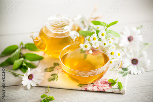 Chamomile flower tea in a glass cup and teapot, on a wooden table.