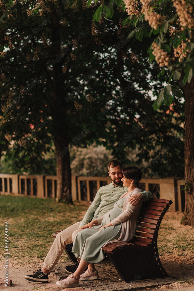 Fototapeta premium Husband with his pregnant wife walking in park. Happy family concept photo. No focus blurred and noise effect