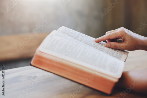 Fotografie, Obraz Close up of a woman hand  hold and pointing  the open bible, blurred page on woo