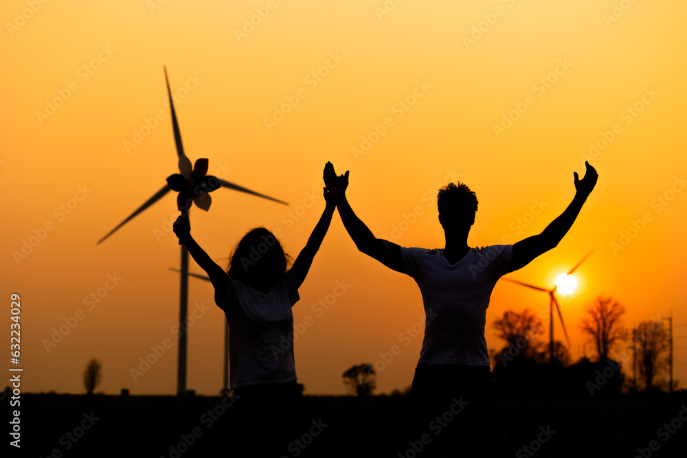 silhouette Hispanic brazillian couple standing together in front of wind turbine. Wind turbines for electric power and energy. Sustainable electricity production. Happy sucess hand up silhouette Hispanic brazillian couple standing together in front of wind turbine. Wind turbines for electric power and energy. Sustainable electricity production. Happy sucess hand up