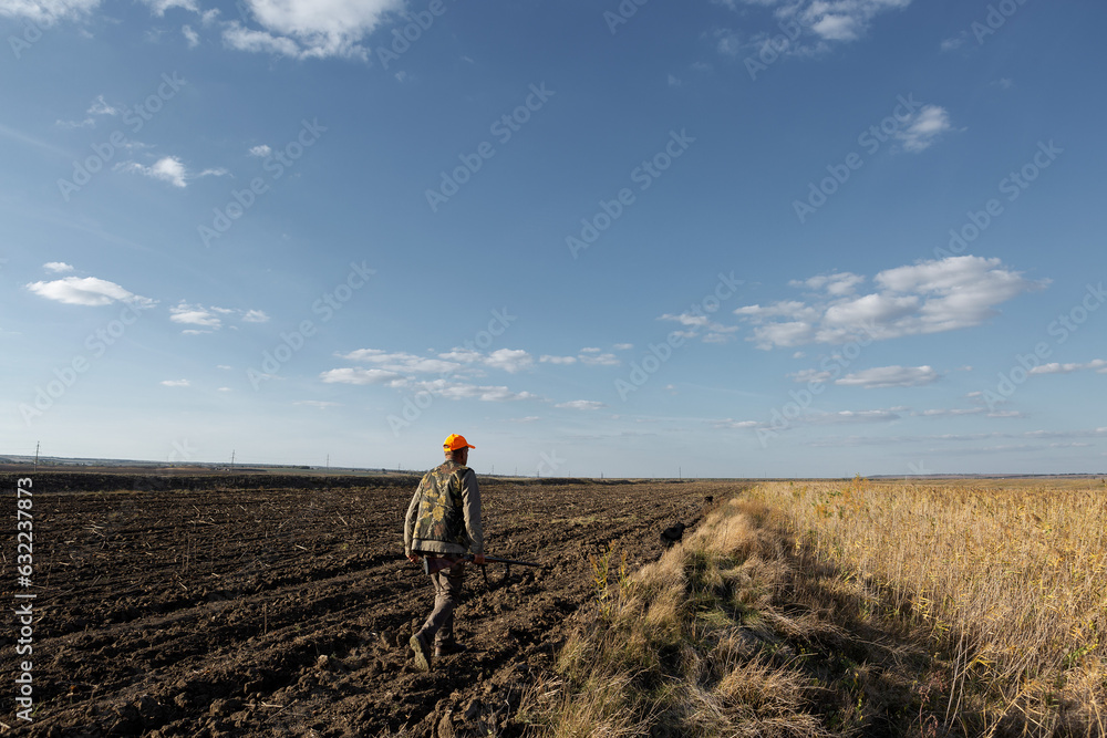 Fototapeta premium Mature man hunter with gun while walking on field.