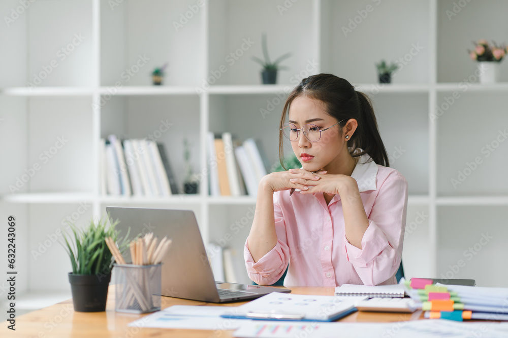 An Asian businesswoman is using a laptop computer and working with a calculator and documents, conducting financial planning for investments and analyzing the financial report. An Asian businesswoman is using a laptop computer and working with a calculator and documents, conducting financial planning for investments and analyzing the financial report.