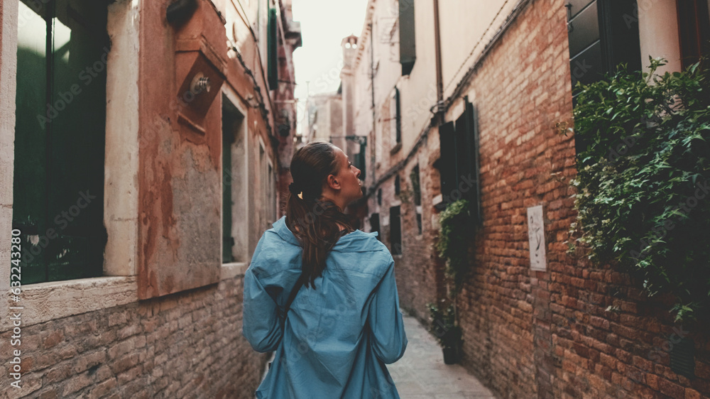 Young woman walking along narrow street of old city, Venice, Back view