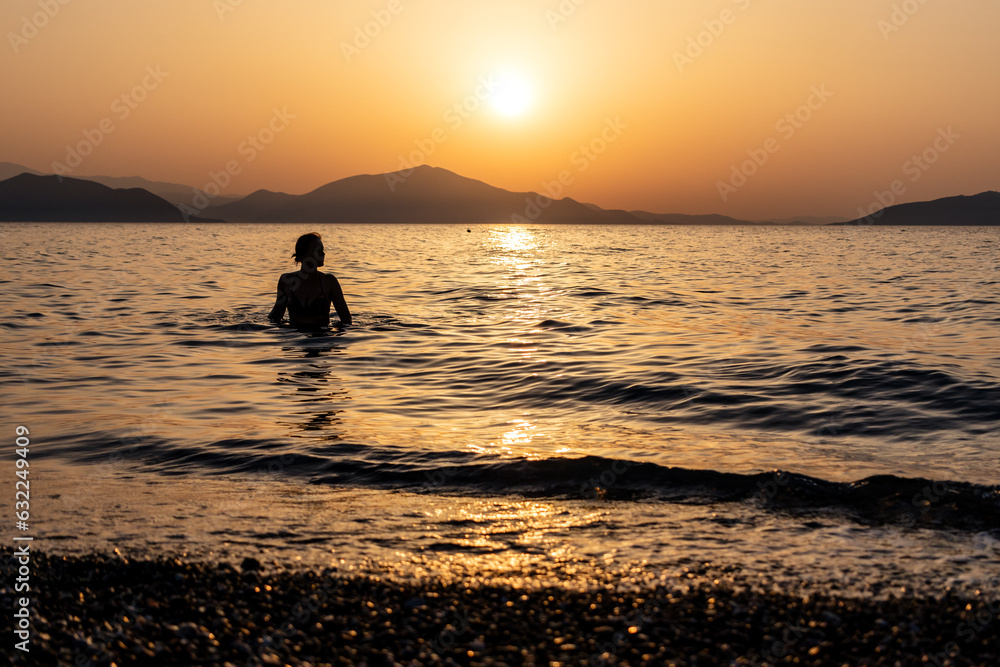Silhouette of a woman entering the sea or ocean at sunset. Copy space.