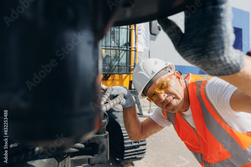 Man in hard hat industrial worker Machinery tractor mechanic checks hydraulic hose system equipment on excavator © Parilov
