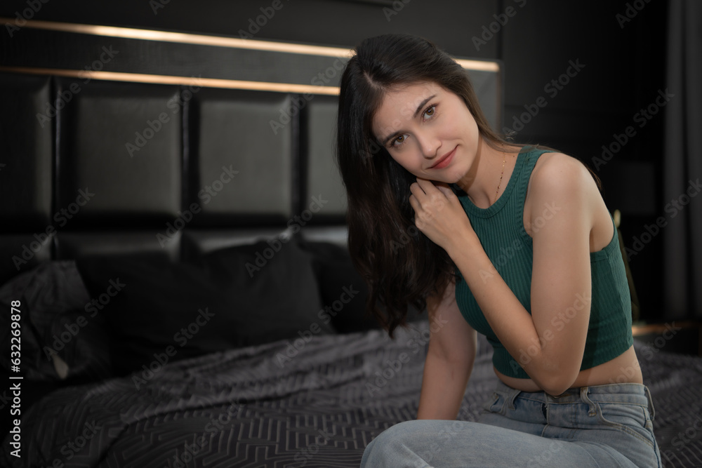 Young woman sitting on the bed in the room at night time. Young woman sitting on the bed in the room at night time.