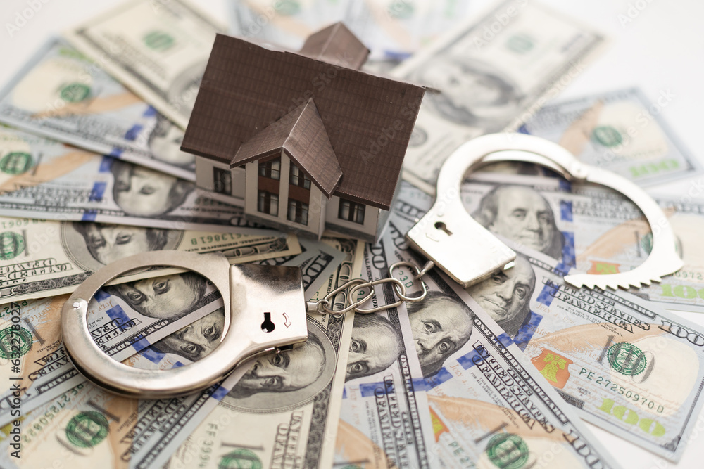 handcuffs, a model of a wooden house against a background of banknotes. crimes in real estate. handcuffs, a model of a wooden house against a background of banknotes. crimes in real estate.