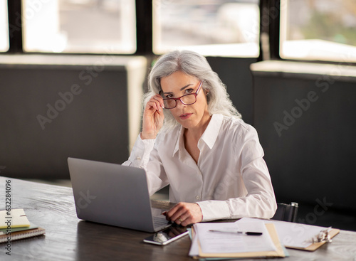 Serious Businesswoman Looking At Camera Through Glasses At Workplace Indoors