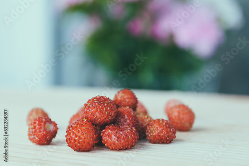 Woodland Strawberry. Heap of ripe red delicious wild berries (Fragaria vesca) on colorful background. Closeup of alpine strawberry on wooden table. Macro shot.