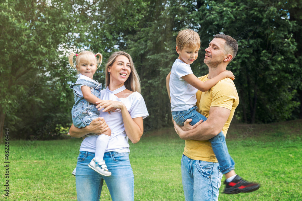 Obraz premium Family with children in the park. Mom, dad, son and little daughter in jeans and white t-shirts laugh and hug. Love and tenderness.