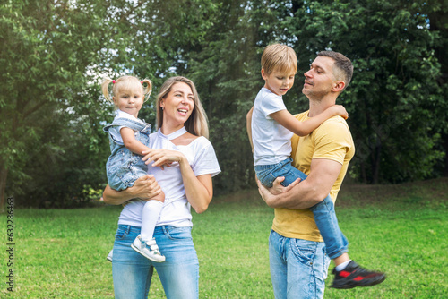 Family with children in the park. Mom, dad, son and little daughter in jeans and white t-shirts laugh and hug. Love and tenderness. © Анна Демидова