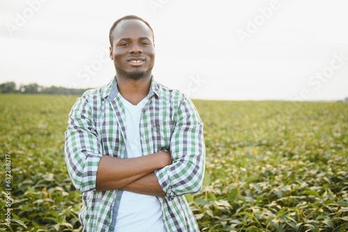 Farmer is standing in his growing soybean field. He is satisfied because of good progress of plants.