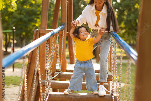 Japanese Mother Helping Little Baby Walk Swinging Bridge On Playground