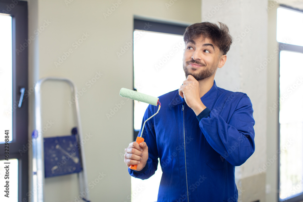 young handsome man smiling with a happy, confident expression with hand on chin. painting home concept young handsome man smiling with a happy, confident expression with hand on chin. painting home concept