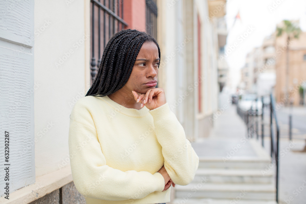 afro pretty black woman feeling confused or doubting, concentrating on an idea, thinking hard, looking to copy space on side