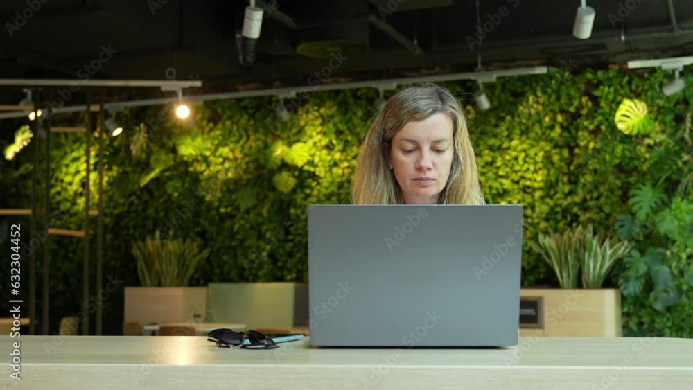 Woman using laptop in coworking with green plants. Female freelancer typing on laptop keyboard. Online work in cafe Woman using laptop in coworking with green plants. Female freelancer typing on laptop keyboard. Online work in cafe