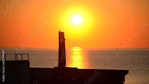 Sunset dawn on sea near pier. Black silhouette of pier on background of sunset dawn on sea in summer morning evening. Sea natural landscape. Sunny nature scenery. Sundown sunshiny Sunrise seascape photo