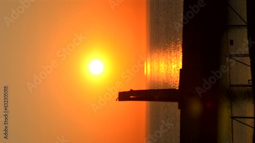 Sunset dawn on sea near pier. Black silhouette of pier on background of sunset dawn on sea in morning evening. Sea natural landscape. Sunny nature scenery. Sundown sunshiny Sunrise seascape Vertical