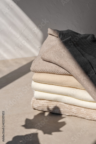 Obraz na plátně Stack of beige, taupe, white, light brown knitted sweaters on neutral beige background with aesthetic lifestyle sunlight shadows