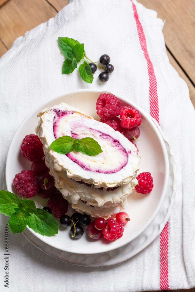 Meringue roll with whipped cream and currant curd, served with berries on a ceramic plate. Rustic style.