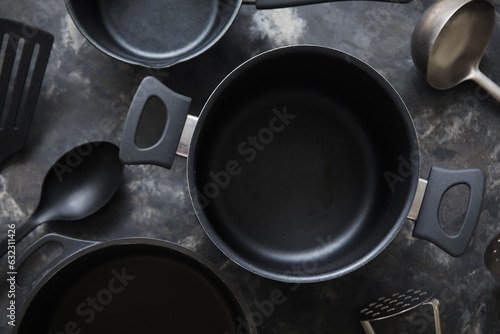 Cooking pots and kitchen utensils on dark grunge background, closeup