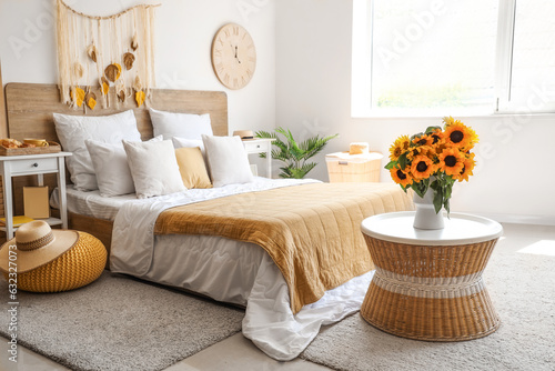 Interior of light bedroom with sunflowers in vase on table