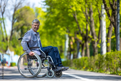 Handicapped man in wheelchair riding on street road, outdoor leisure for disable guy. © zinkevych