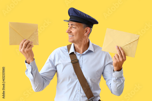 Mature postman with envelopes on yellow background photo