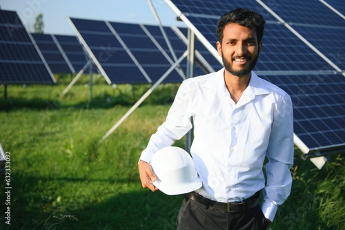 Male arab engineer standing on field with rows of solar panels. © Serhii