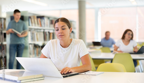 Positive young lady in casual clothes working remotely using a computer in a quiet library