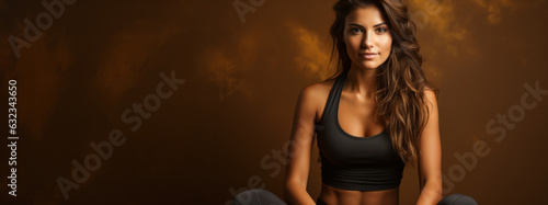 Beautiful sporty woman sit in sportswear on a brown background.
