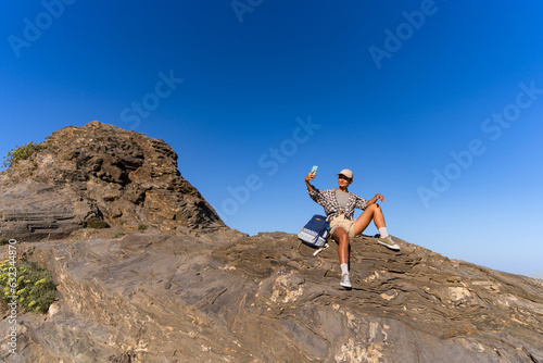 tourist girl with a backpack in the summer on top of a mountain takes a selfie against the backdrop of the sea and mountains