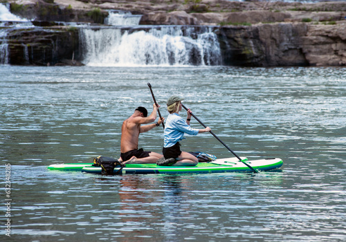 Couple on SUP boards in front of waterfall; Stand up Paddle Boards 