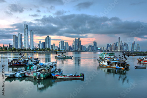 Futuristic skyline of Panama city at sunset against fishing boats reflecting in the still water.