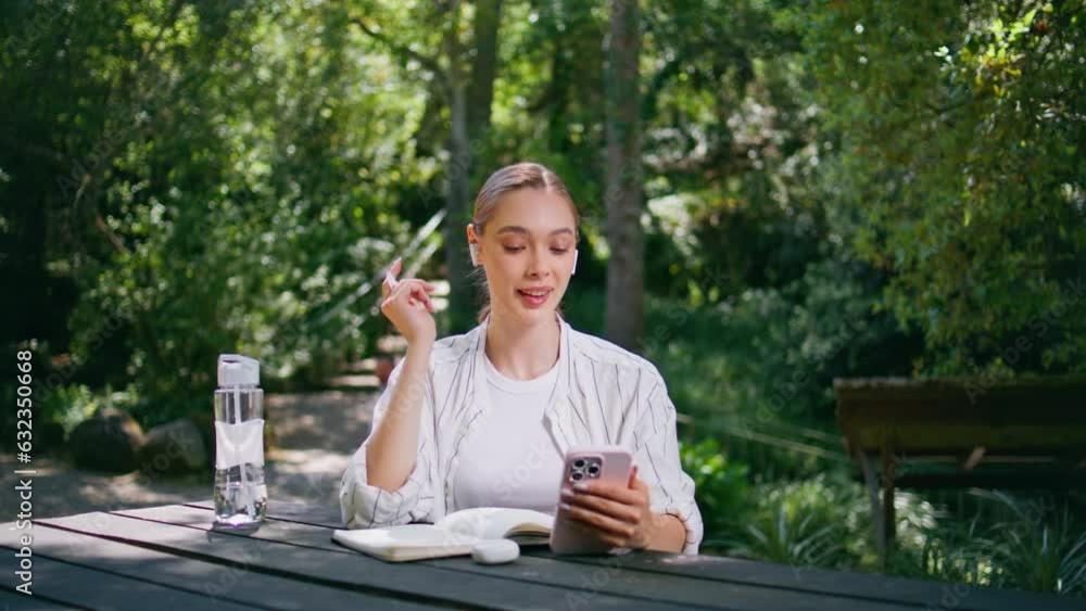 Happy woman headphones answering video call at smartphone on park table close up Happy woman headphones answering video call at smartphone on park table close up