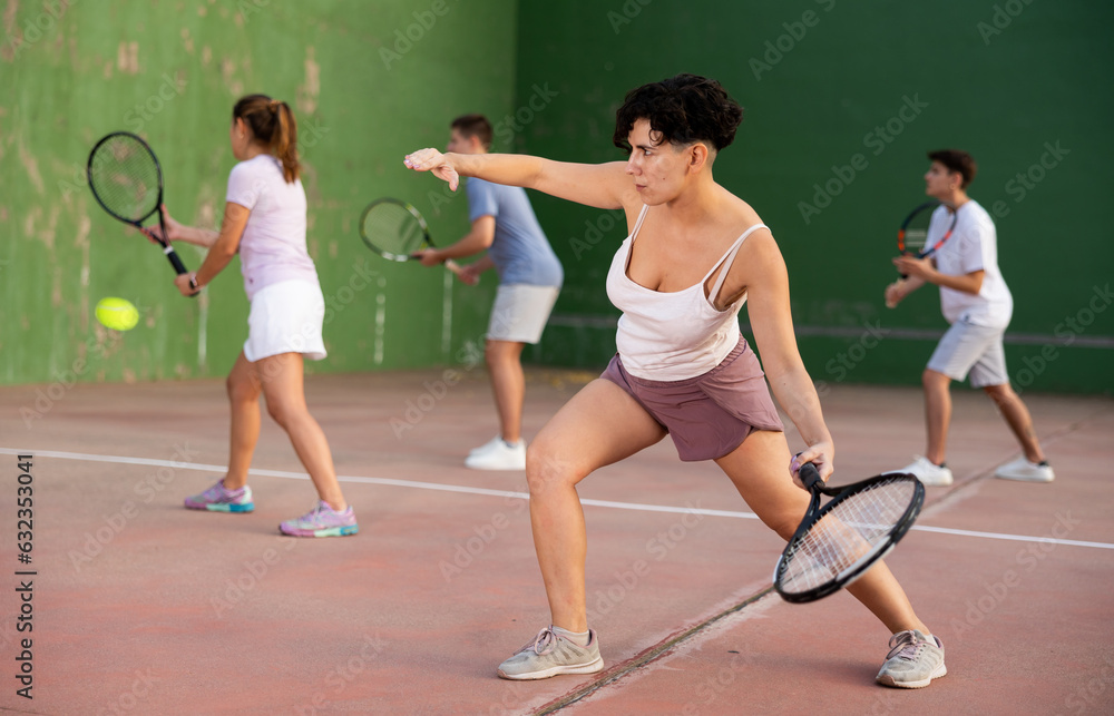 Latin woman serving ball during frontenis game outdoors. Woman playing pelota on outdoor fronton.