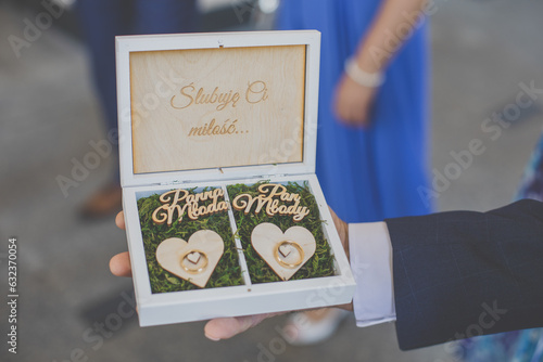 Drewniane pudełko z obrączkami ślubnymi. Drewniana skrzynka z napisem "Ślubuję ci miłość...". Pierścionki w mchu. Wooden box with wedding rings. A wooden box with the inscription "I swear to you love.