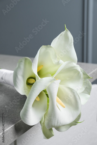 Fototapeta Naklejka Na Ścianę i Meble -  Beautiful calla lily flowers tied with ribbon on grey table, closeup
