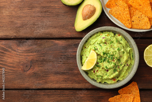 Bowl of delicious guacamole and nachos chips on wooden table, flat lay. Space for text