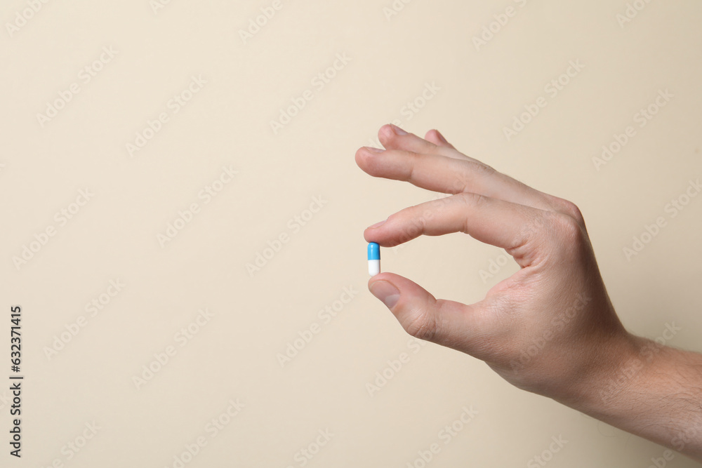 Man holding pill on beige background, closeup. Space for text Man holding pill on beige background, closeup. Space for text